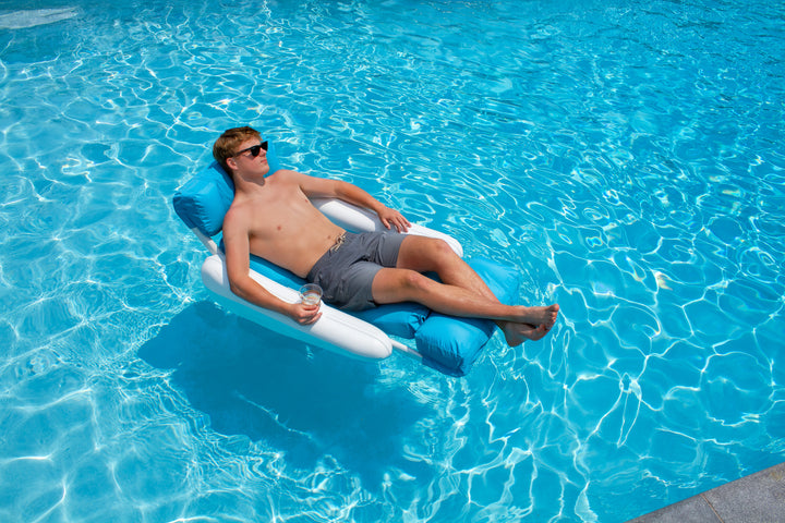 man wearing sunglasses lounging on a blue and white Swimline Sunchaser Sunsoft luxury pool lounger floating in clear blue pool water with a drink in hand