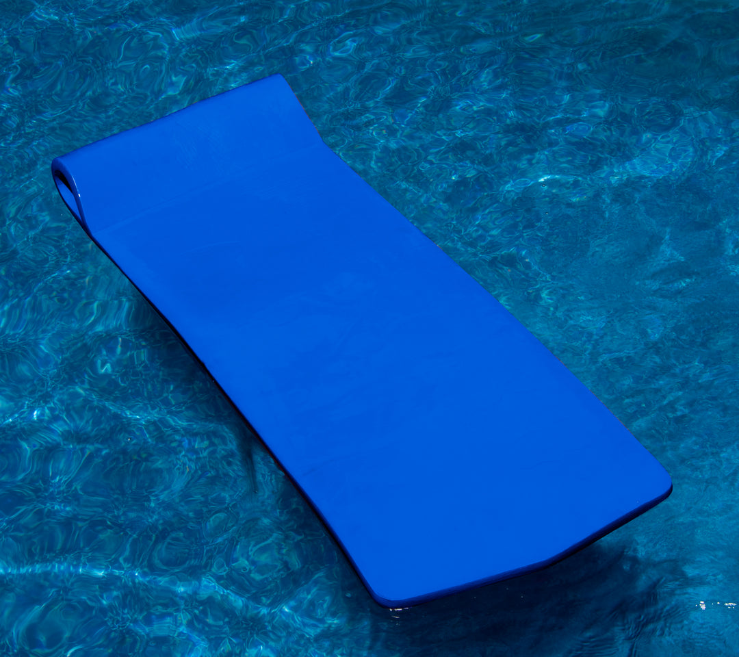 Swimline Sofskin floating mattress in bright blue floating on clear pool water showing smooth flat sleeping surface and rounded edges