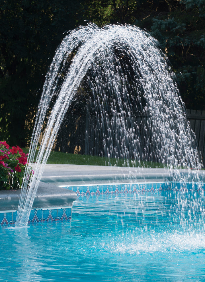 Water fountain spraying two clear water arches over a bright blue swimming pool near concrete edge with colorful tile border