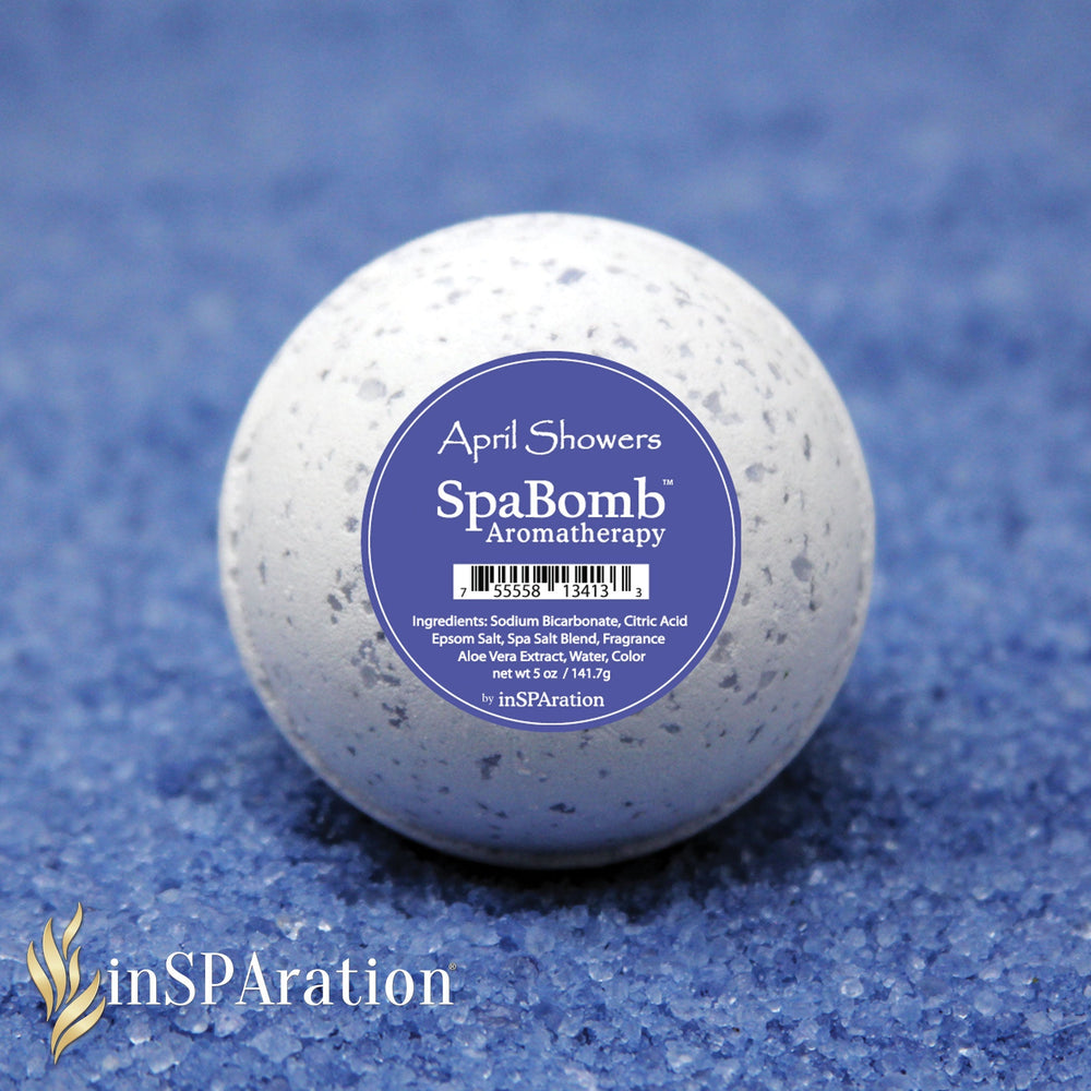inSPAration SpaBomb aromatherapy bath bomb in white with grey speckles and blue label reading April Showers on blue textured surface