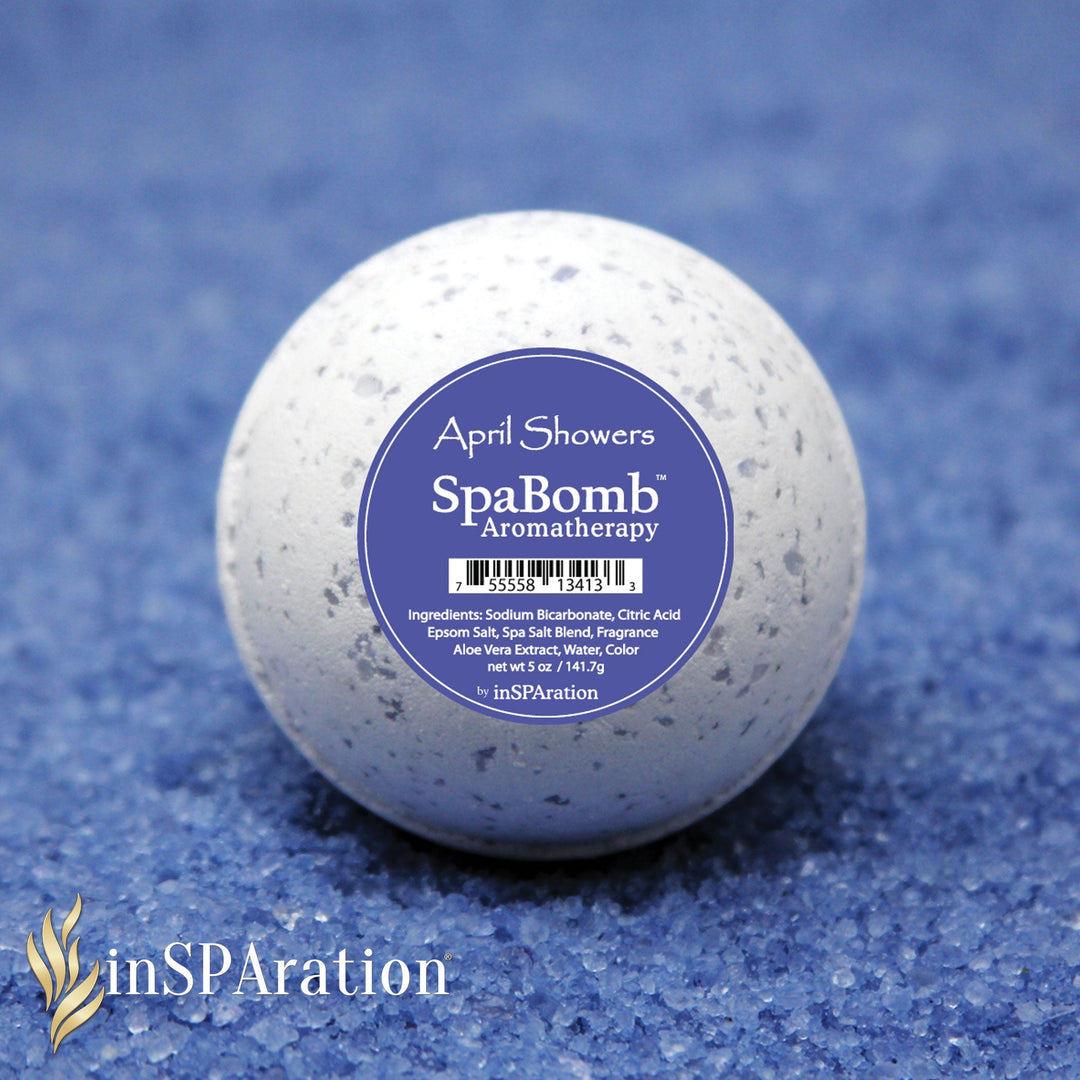 inSPAration SpaBomb aromatherapy bath bomb in white with grey speckles and blue label reading April Showers on blue textured surface