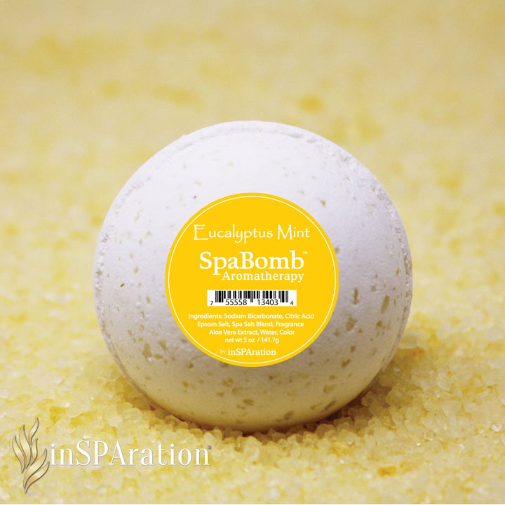 inSPAration SpaBomb Aromatherapy eucalyptus mint bath bomb in white with small textured specks resting on coarse yellow bath salt crystals