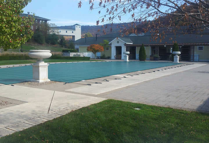 GLI 20 by 40 foot green rectangle mesh safety pool cover installed over an outdoor pool secured with black straps and anchors