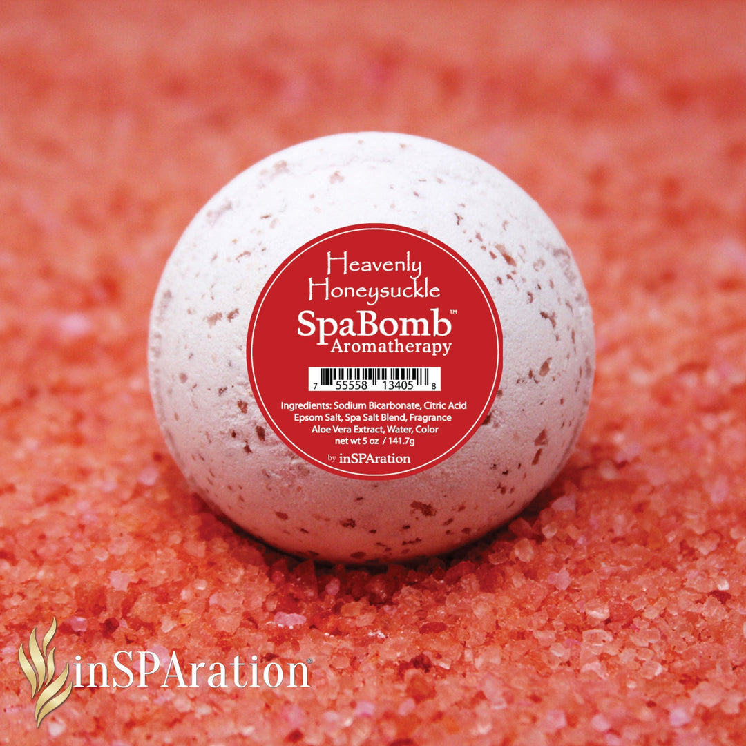 round white speckled inSPAration SpaBomb Aromatherapy bath bomb with red label resting on coarse pink bath salt crystals