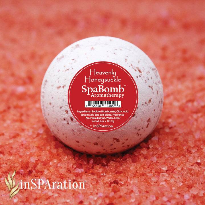 round white speckled inSPAration SpaBomb Aromatherapy bath bomb with red label resting on coarse pink bath salt crystals