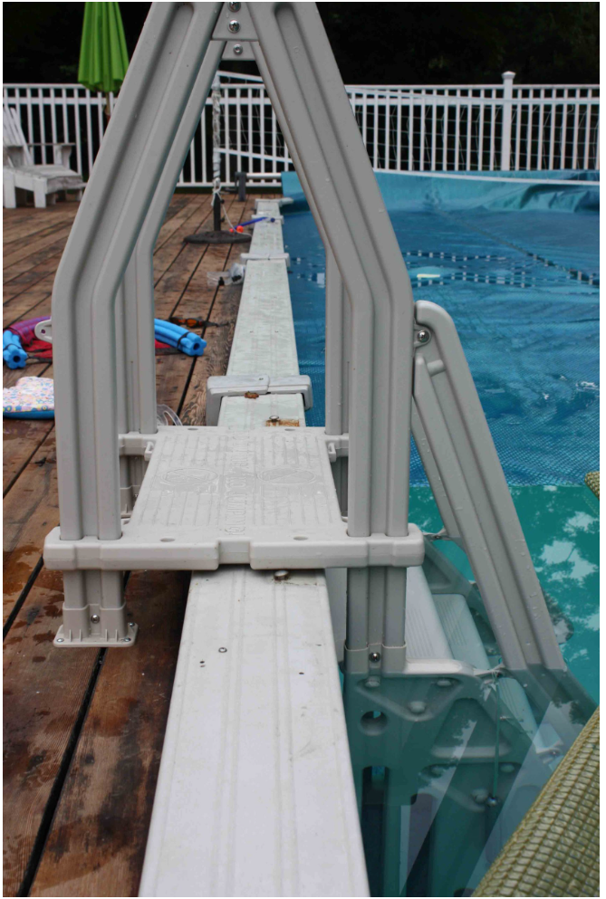 white vinyl pool drop in step installed on wooden deck next to blue pool with arm rails and textured top surface