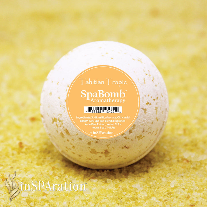 inSPAration SpaBomb Aromatherapy bath bomb with white and beige speckled surface and orange label on sandy yellow background