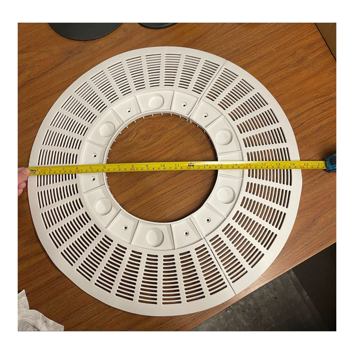 white circular pool drain outlet cover with multiple slotted vents and a measuring tape stretched across its diameter on a wooden surface