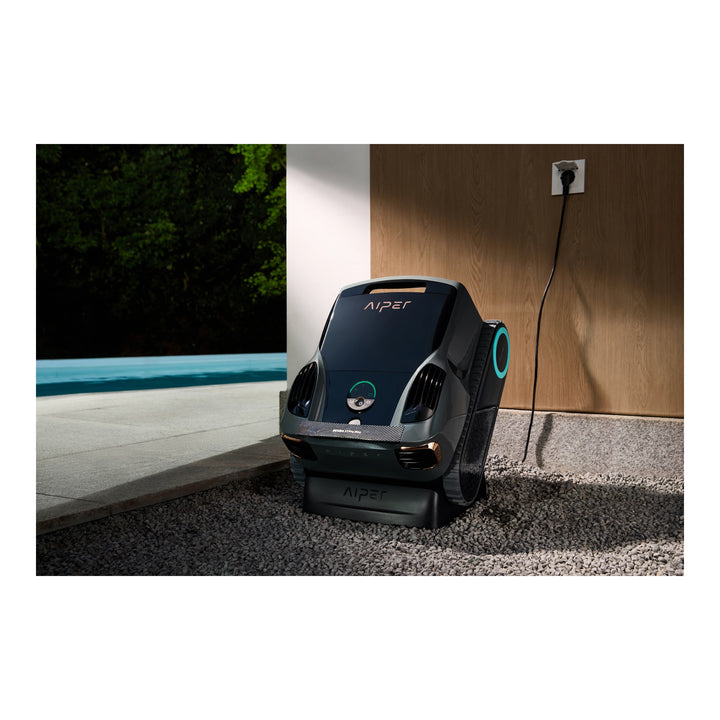 Aiper Scuba X1 Pro Max cordless robotic pool cleaner on charging dock, resting on gravel near a pool.